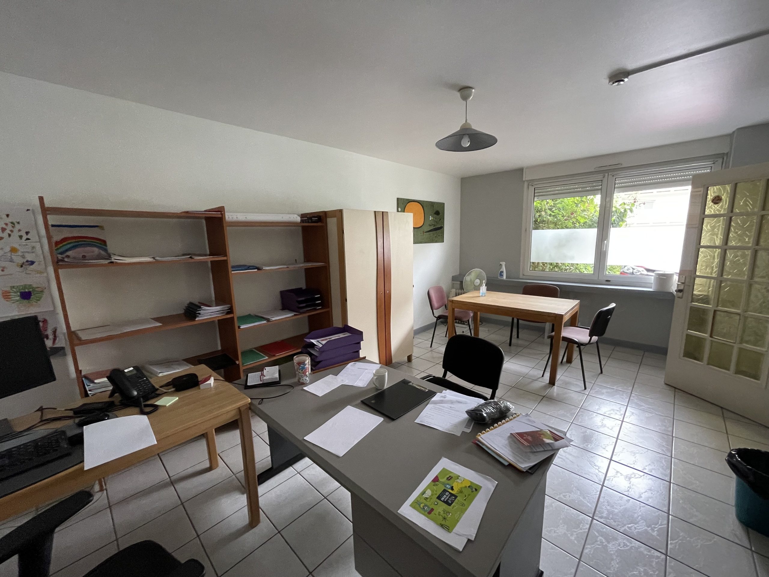 Bureau professionnel de la MECS de l'Allée Neuve, montrant un bureau avec des chaises, des étagère, une table et des chaises, avec une fenêtre donnant sur un extérieur verdoyant