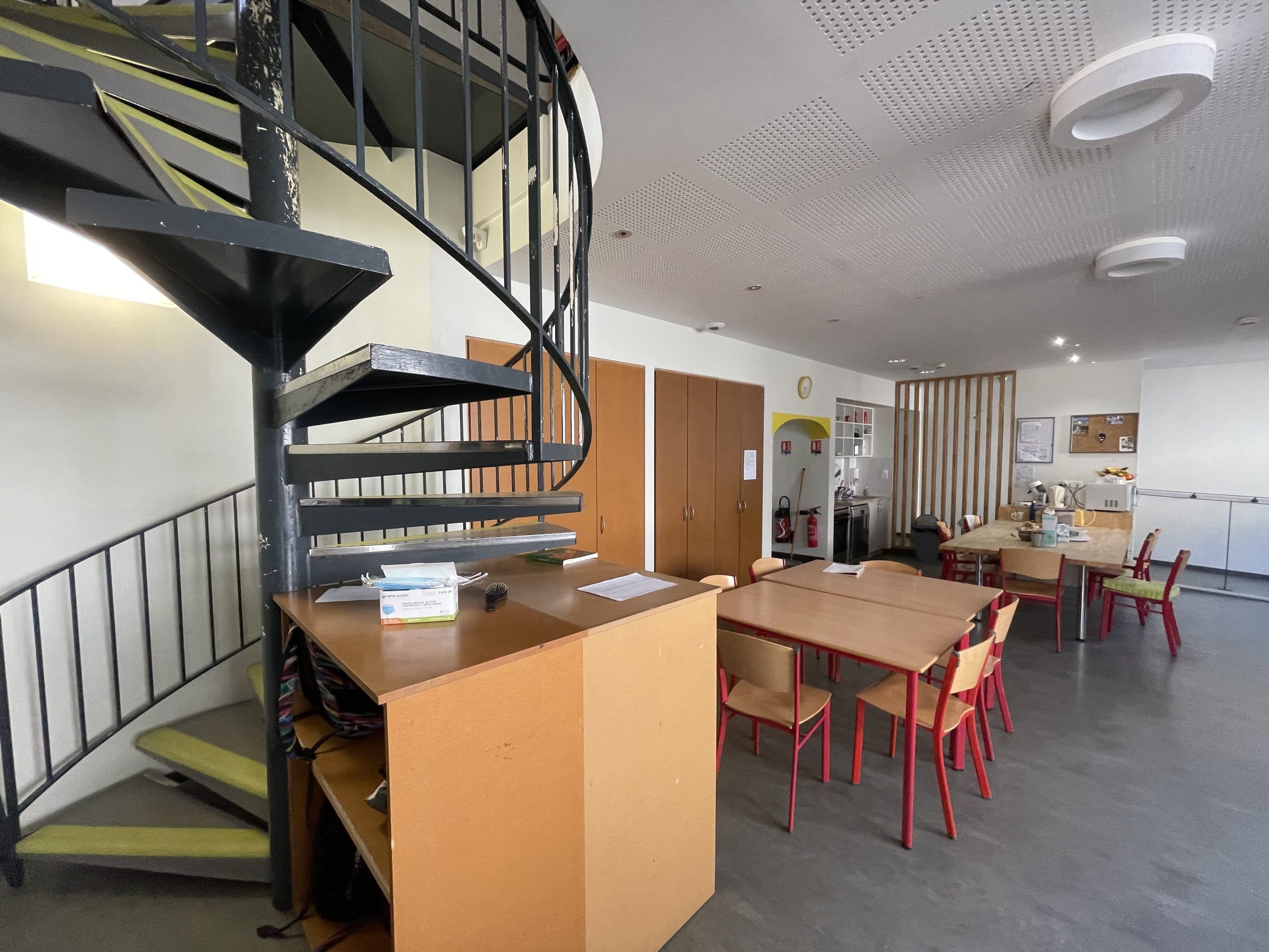 Salle de vie commune de la MECS de Han-sur-Seille, montrant une cuisine ouverte sur une salle à manger, avec des tables et des chaises, et d'un escalier pour l'accès à un étage supérieur