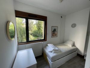 Chambre individuelle du SHERPA, montrant un lit, une table, un miroir, avec une fenêtre donnant sur un extérieur verdoyant